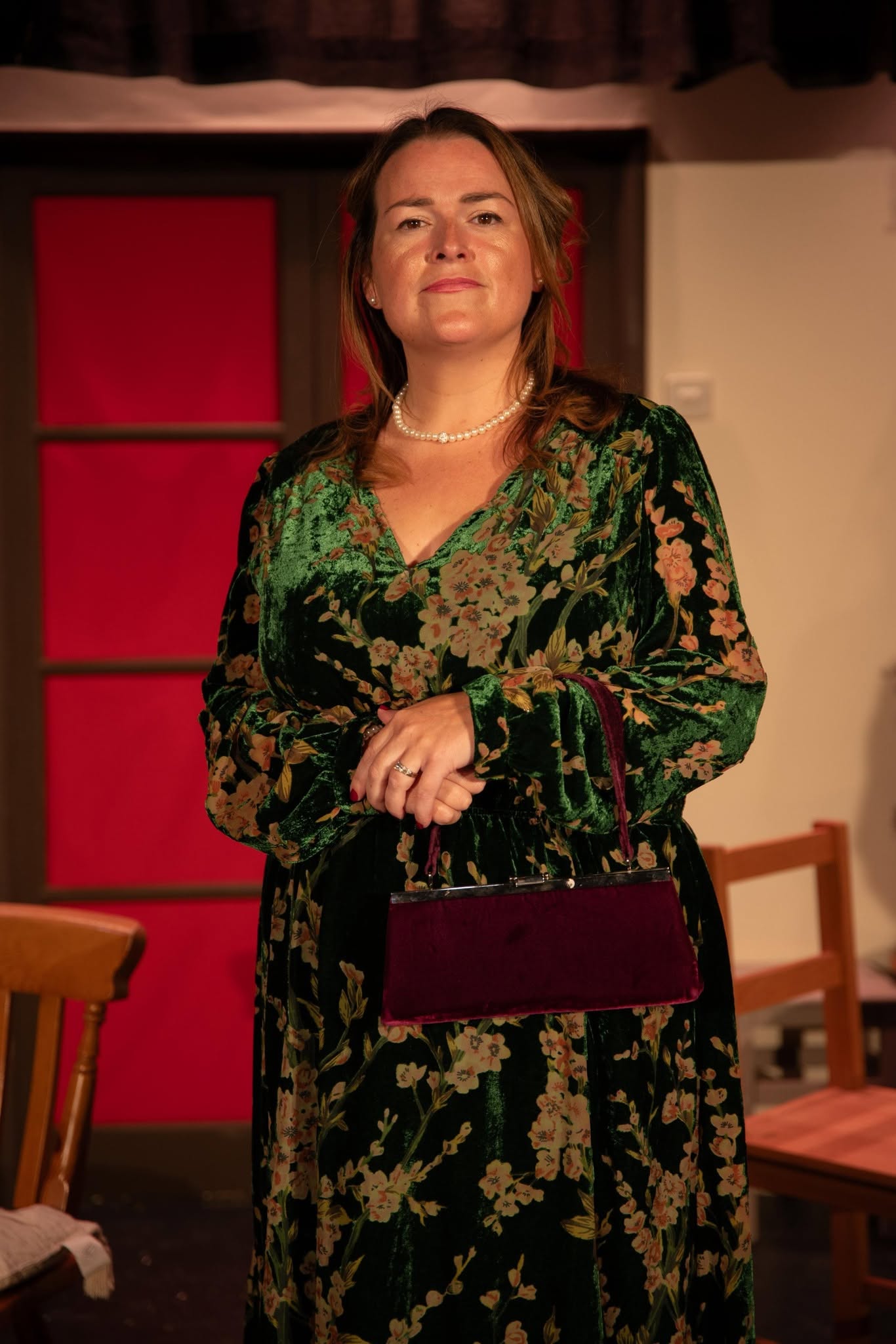 A Blithe Spirit cast member in a green floral costume holding a handbag